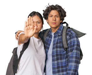 Young interracial student couple studying standing with outstretched hand showing stop sign, preventing you.