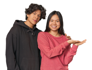 Young interracial couple in studio holding a copy space on a palm.