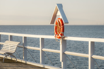 A weathered wooden bench sits on a pier overlooking a vast expanse of the ocean. A bright orange...