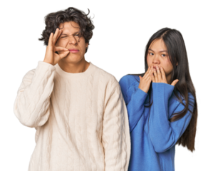 Young interracial couple in studio with fingers on lips keeping a secret.