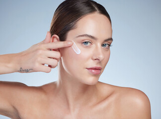 Woman, portrait and application of cream in studio, hydration and smooth beauty on blue background. Female person, cosmetics and lotion for facial treatment, skincare and hyaluronic acid moisturizer
