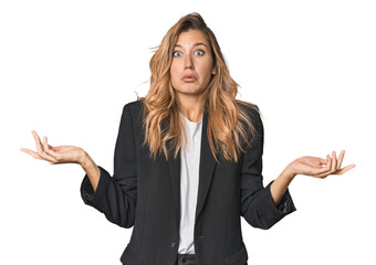 Young businesswoman in a suit doubting and shrugging shoulders in questioning gesture.