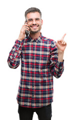 Young hipster adult man talking on the phone very happy pointing with hand and finger to the side