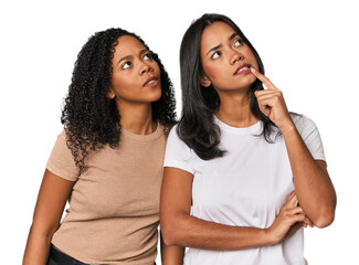 Young Latin friends in studio looking sideways with doubtful and skeptical expression.