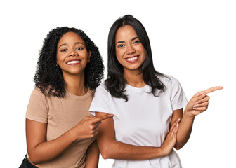 Young Latin friends in studio smiling cheerfully pointing with forefinger away.