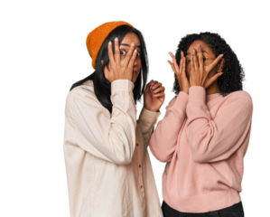 Young Latin friends together in studio blink through fingers frightened and nervous.