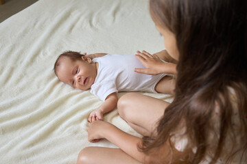 Unrecognizable older child welcomes her new sibling. Adorable girl and the newborn baby boy lie on a bed in the bedroom on white sheet copy space for promotional text