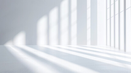 Obraz premium A bright empty room with white walls and floor, illuminated by natural light streaming through large windows, casting soft shadows.