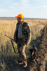 Mature man hunter with gun while walking on field.
