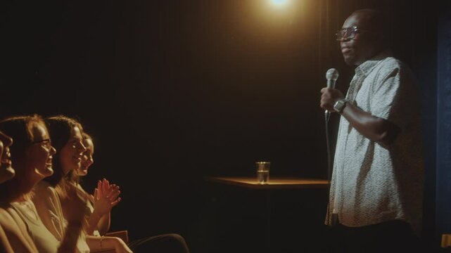 Young cheerful people in audience laughing and applauding to African American comedian performing on stage in stand-up club