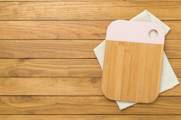 Cutting board with napkin on wooden background, top view