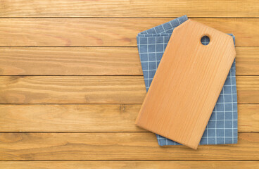Cutting board with napkin on wooden background, top view