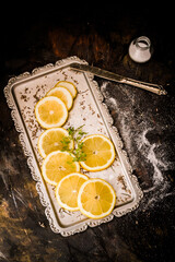 Lemon slices on a silver tray with a knife and a small jar of salt on a dark background with...