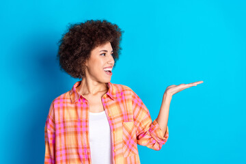 Photo portrait of attractive young woman look excited hold empty space dressed stylish checkered clothes isolated on blue color background