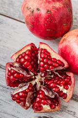 Pomegranate fruit cut open to reveal its juicy red seeds, whole pomegranates on a white wooden surface.