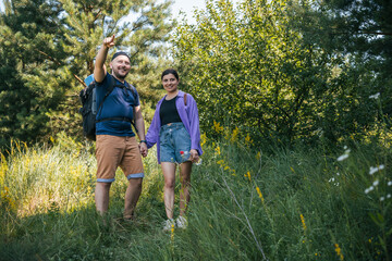 Happy couple tourists with backpacks walking outdoors in the summer forest