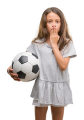 Brunette hispanic girl holding soccer football ball cover mouth with hand shocked with shame for mistake, expression of fear, scared in silence, secret concept