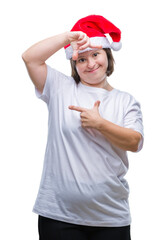 Young adult woman with down syndrome wearing christmas hat over isolated background smiling making frame with hands and fingers with happy face. Creativity and photography concept.