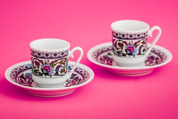 Elegant porcelain Turkish coffee cups with decorative pattern on pink background.