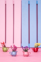Small polka dot vases in different colors of blue, pink, green and red with colorful flowers on a pink surface and striped pink and blue background.