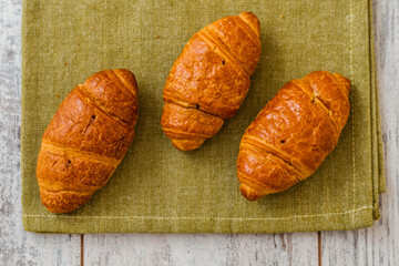 Freshly baked croissants on a green cloth, placed on a rustic white wooden table.