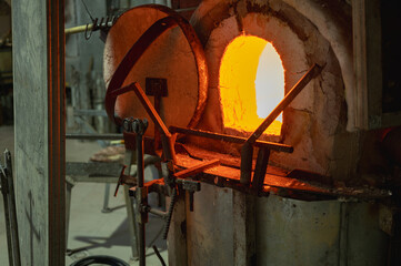 Close-up image of a glassblower forming hot molten glass under intense fire in a workshop, blast...