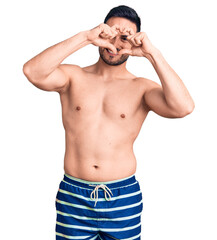 Naklejka premium Young handsome man wearing swimwear doing heart shape with hand and fingers smiling looking through sign