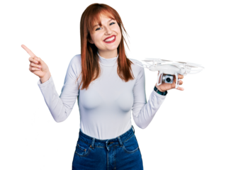 Redhead young woman holding drone smiling happy pointing with hand and finger to the side