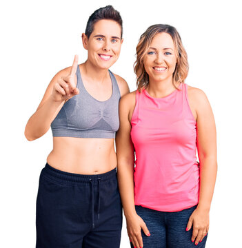 Couple of women wearing sportswear showing and pointing up with finger number one while smiling confident and happy.