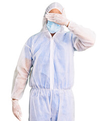 Young hispanic man wearing doctor protection coronavirus uniform and medical mask smiling and laughing with hand on face covering eyes for surprise. blind concept.