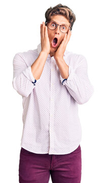 Young handsome man wearing business clothes and glasses afraid and shocked, surprise and amazed expression with hands on face