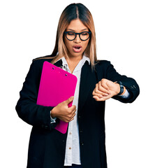 Young hispanic business woman holding clipboard with blank space looking at the watch time worried, afraid of getting late