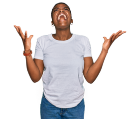 Young african american woman wearing casual white t shirt crazy and mad shouting and yelling with aggressive expression and arms raised. frustration concept.