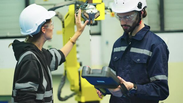 Technician man hold controller pad of robotic arm machine and work with co-worker woman check and maintenance in factory workplace.