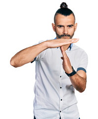 Hispanic man with ponytail wearing casual white shirt doing time out gesture with hands, frustrated...