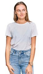 Beautiful young blonde woman wearing casual white t shirt smiling looking to the side and staring away thinking.