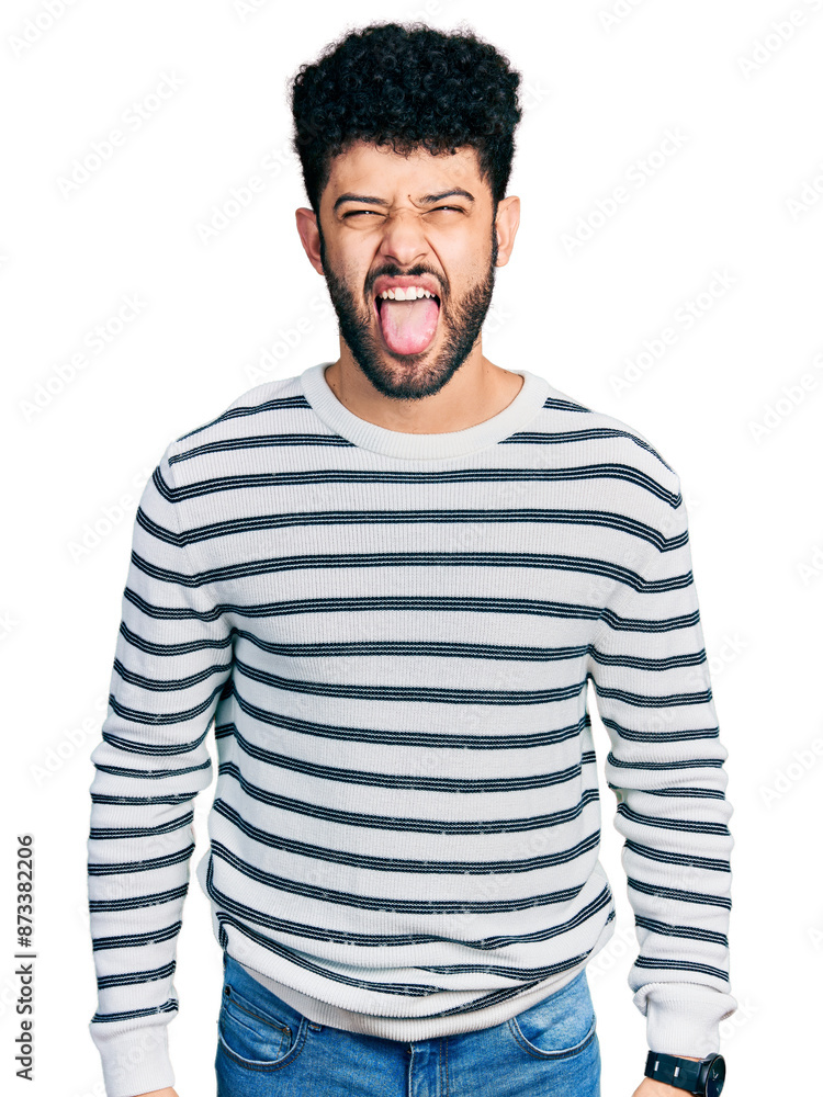 Poster young arab man with beard wearing casual striped sweater sticking tongue out happy with funny expres