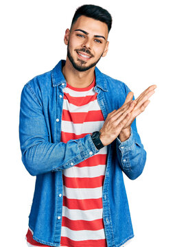 Young hispanic man with beard wearing casual denim jacket clapping and applauding happy and joyful, smiling proud hands together