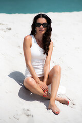 Luxury fashion woman in white dress and sunglasses on the white sand beach