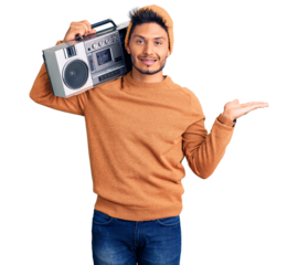 Handsome latin american young man holding boombox, listening to music smiling cheerful presenting and pointing with palm of hand looking at the camera.