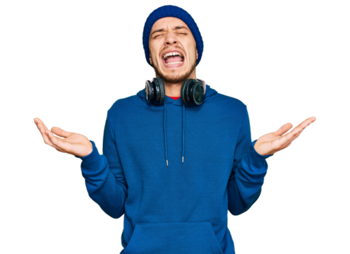 Hispanic young man wearing sweatshirt and wool hat celebrating mad and crazy for success with arms raised and closed eyes screaming excited. winner concept