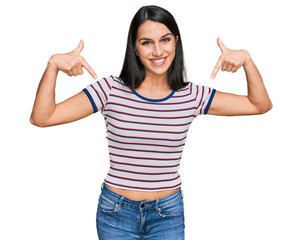 Young hispanic girl wearing casual striped t shirt looking confident with smile on face, pointing...