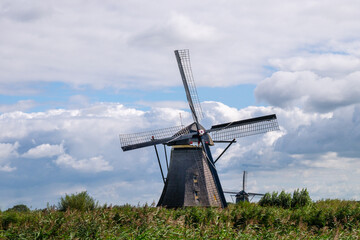 Fototapeta premium A windmill is standing in a field with a cloudy sky in the background