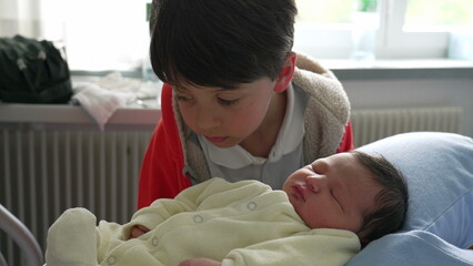 Older Brother Gently Kissing Newborn Baby's Cheek and mother in a Warm, Loving Family Moment, hospital with Natural Light