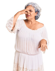 Senior woman with gray hair wearing bohemian style smelling something stinky and disgusting,...