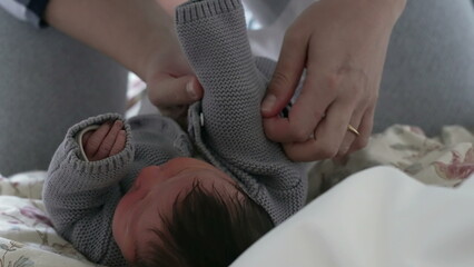 Parent putting a cozy grey sweater on a newborn, illustrating the careful and loving attention...