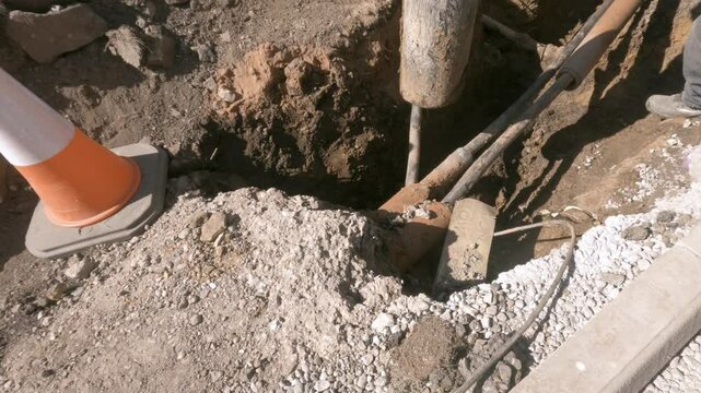 Worker Inspecting Underground Cables Near Curb During Roadwork