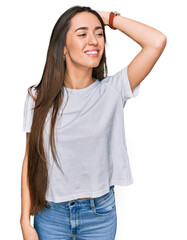 Fototapeta premium Young hispanic girl wearing casual white t shirt smiling confident touching hair with hand up gesture, posing attractive and fashionable