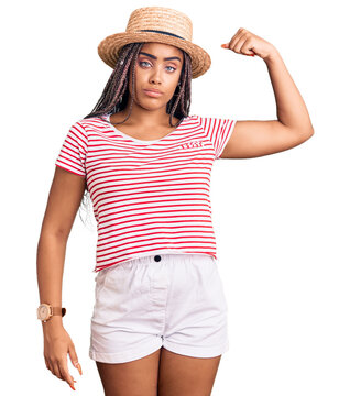 Young african american woman with braids wearing summer hat strong person showing arm muscle, confident and proud of power