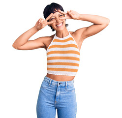 Young brunette woman with short hair wearing casual clothes doing peace symbol with fingers over...